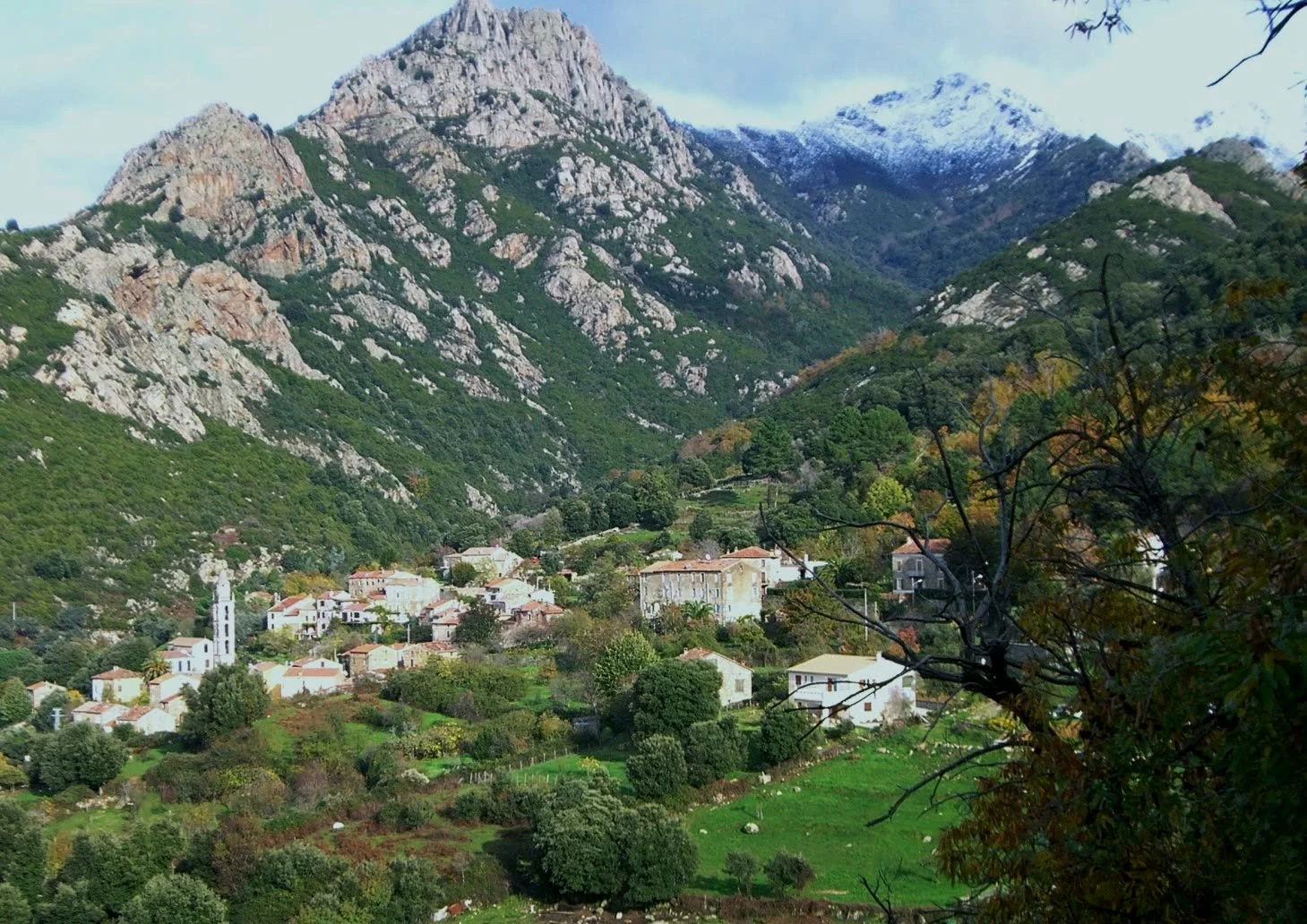 Le village de Peri et son clocher dans la vallée, au pied de montagnes rocheuses